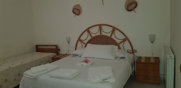 A neatly made bed with white linens and towels, a wooden headboard, bedside tables, and a small dresser.
