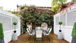 A patio with a table and chairs, surrounded by white walls and covered with greenery. - Village Serenity, by Veeve (London)