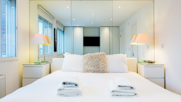 A modern hotel room with a large bed, two bedside tables, a mirror, and two lamps. - Village Serenity, by Veeve (London)