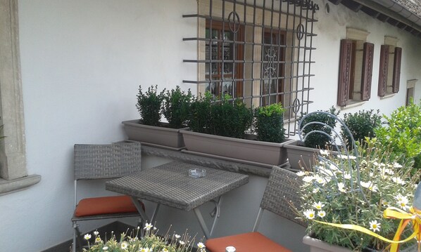 A small outdoor seating area with a table and two chairs, surrounded by potted plants and flowers.