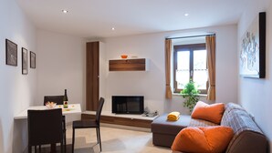 A modern living room with a dining area, a flat-screen TV, and a sofa with orange cushions. - Apartment in the center of St. Pauls - Appiano - near Caldaro and Bolzano (Pauls)