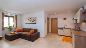 A modern living room with a sectional sofa, a small dining table, and a kitchen area with wooden cabinets and a sink. - Apartment in the center of St. Pauls - Appiano - near Caldaro and Bolzano (Pauls)