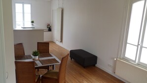 A dining area with a wooden table, chairs, and a bench. There is a radiator on the wall and a window with a view. - Magnificent apartment (80 m²) with 4 main rooms, 100 meters from the beach (Hermanville-Sur-Mer)