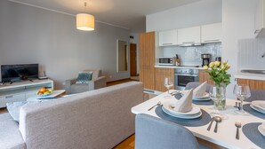 A modern living room with a sofa, a dining table set for two, and a kitchen area with cabinets and appliances.