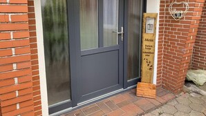 En mørk dør med et matteret glasfelt, et træskilt med tekst og en hjerteformet dekoration på væggen.