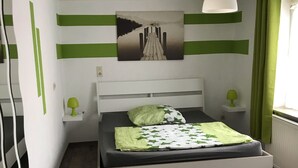 Et soveværelse med en seng, grønne gardiner, et maleri og en hængende lampe.