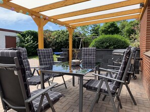 An outdoor patio with a glass table surrounded by chairs with plaid cushions. - Holiday adjacent to the farm (Leer (Ostfriesland))