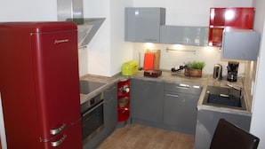 Une cuisine de taille réduite avec des meubles gris, un réfrigérateur rouge et un petit espace pour l’évier.