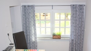 Une pièce avec une fenêtre, un radiateur, une table recouverte d’une nappe à rayures, une chaise et un grille-pain.