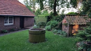 Une maison en briques avec un toit recouvert de tuiles rouges, un jardin bien entretenu et un grand tonneau au premier plan.