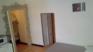 Quarto com cama, guarda-roupa, micro-ondas e porta para outro espaço.