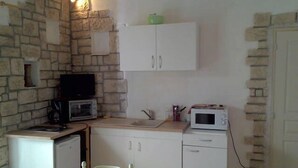 Cozinha compacta com parede de pedra, armários brancos, micro-ondas e uma pia pequena.