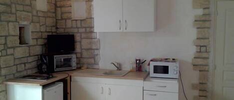 A compact kitchen with a stone wall, white cabinets, a microwave, and a small sink.