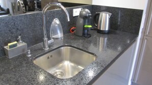 Una cocina con un lavamanos de acero inoxidable, una cafetera y un hervidor sobre la encimera.