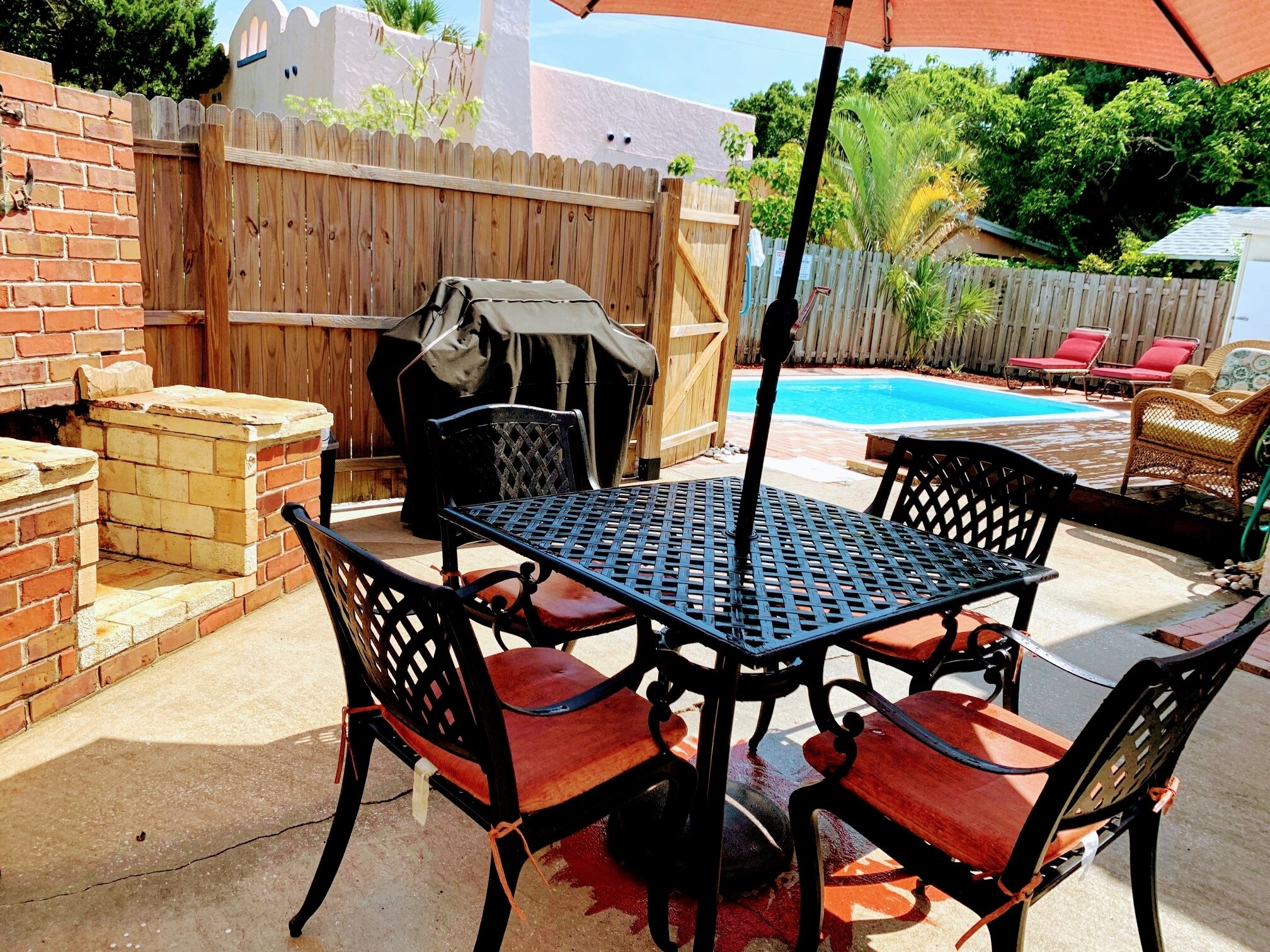 Une terrasse extérieure avec une table et des chaises en métal, un barbecue et une piscine en arrière-plan.