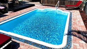A rectangular swimming pool with a tiled edge, surrounded by a brick patio and outdoor furniture including chairs and a lounge chair. - Spanish Style Home With Private Heated Pool (Bradenton)