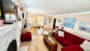 A spacious living room with a red sofa, a wooden coffee table, and a fireplace. There is a dining area with a table and chairs, and a kitchen in the background. - Spanish Style Home With Private Heated Pool (Bradenton)