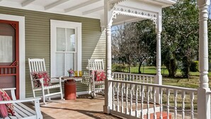 A porch with white railings, a wooden table, and two white chairs with red cushions. - Hollys Haus | 2/2 Cottage | In Town | Private Hot Tub (Fredericksburg)