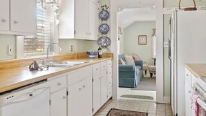 A compact kitchen with white cabinets, a wooden countertop, and a blue and white patterned backsplash. - Hollys Haus | 2/2 Cottage | In Town | Private Hot Tub (Fredericksburg)