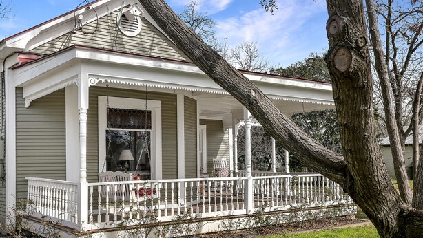 A two-story house with a covered porch, a chimney, and a large tree in front. - Hollys Haus | 2/2 Cottage | In Town | Private Hot Tub (Fredericksburg)