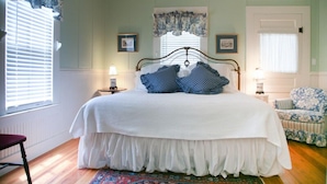 A bedroom with a bed, a chair, a window with blinds, and a door. - Hollys Haus | 2/2 Cottage | In Town | Private Hot Tub (Fredericksburg)