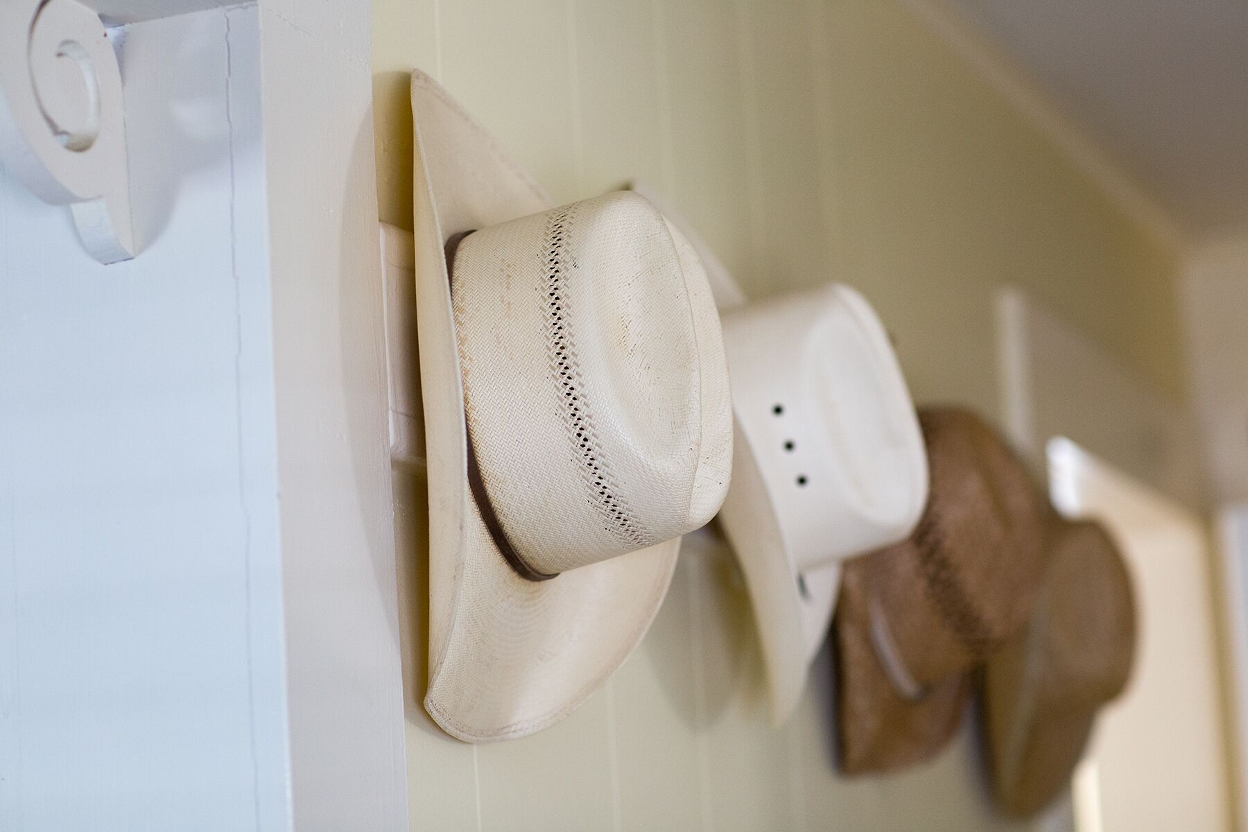 A wall with several hats hanging on hooks.