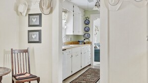 A kitchen with white cabinets, a wooden chair, and a dining table. - Hollys Haus | 2/2 Cottage | In Town | Private Hot Tub (Fredericksburg)