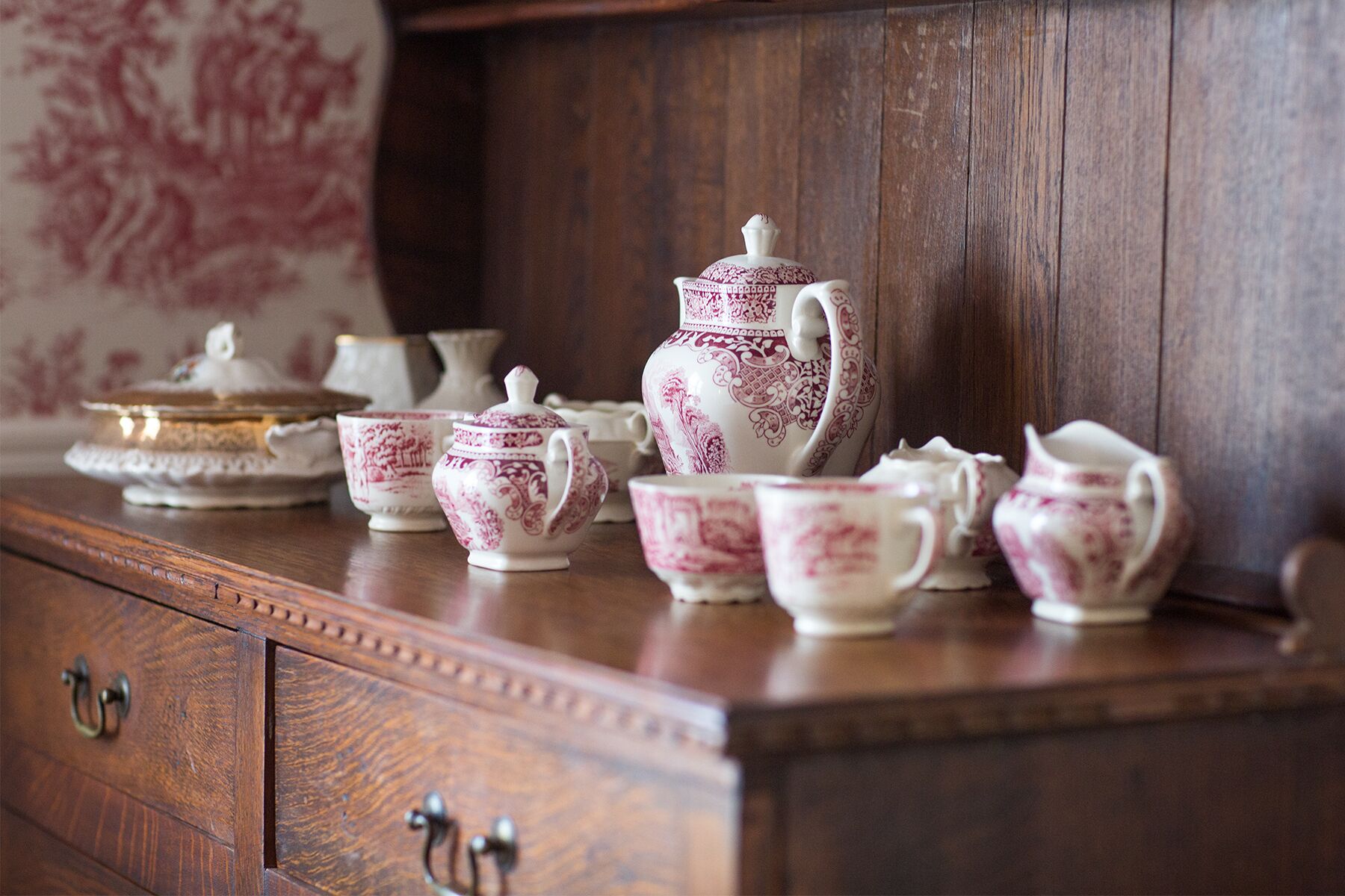 A wooden cabinet with a tea set including cups, saucers, a teapot, and a sugar bowl.