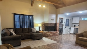 Una sala de estar amplia con un sofá seccional, una chimenea, una cocina con electrodomésticos y un comedor con mesa y sillas.