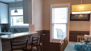 A kitchen with a bar area, wooden chairs, and a dining table with a blue placemat. - Truly Unique! 1938 Historic Beach House (Carolina Beach)