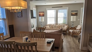 A dining area with wooden chairs and a table, a sofa, and a wicker chair. - Truly Unique! 1938 Historic Beach House (Carolina Beach)