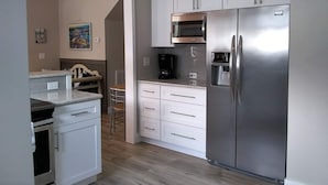 A modern kitchen with white cabinets, a stainless steel refrigerator, a built-in microwave, and a coffee maker. - Truly Unique! 1938 Historic Beach House (Carolina Beach)