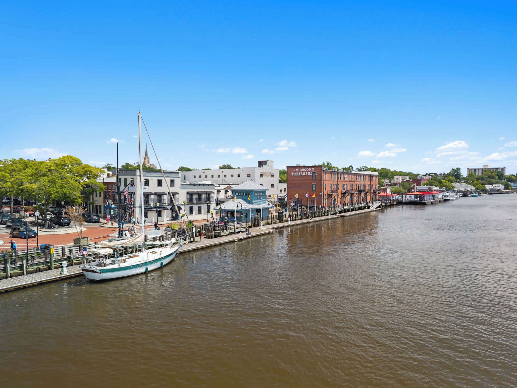 A riverside town with a historic building, a dock with a sailboat, and a bridge.