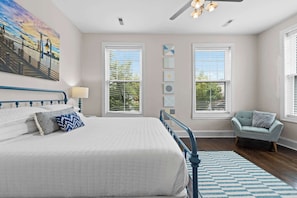 A bedroom with a large bed, two windows, a ceiling fan, and a chair.