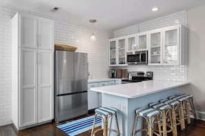A modern kitchen with white cabinetry, stainless steel appliances, and a central island with bar stools.