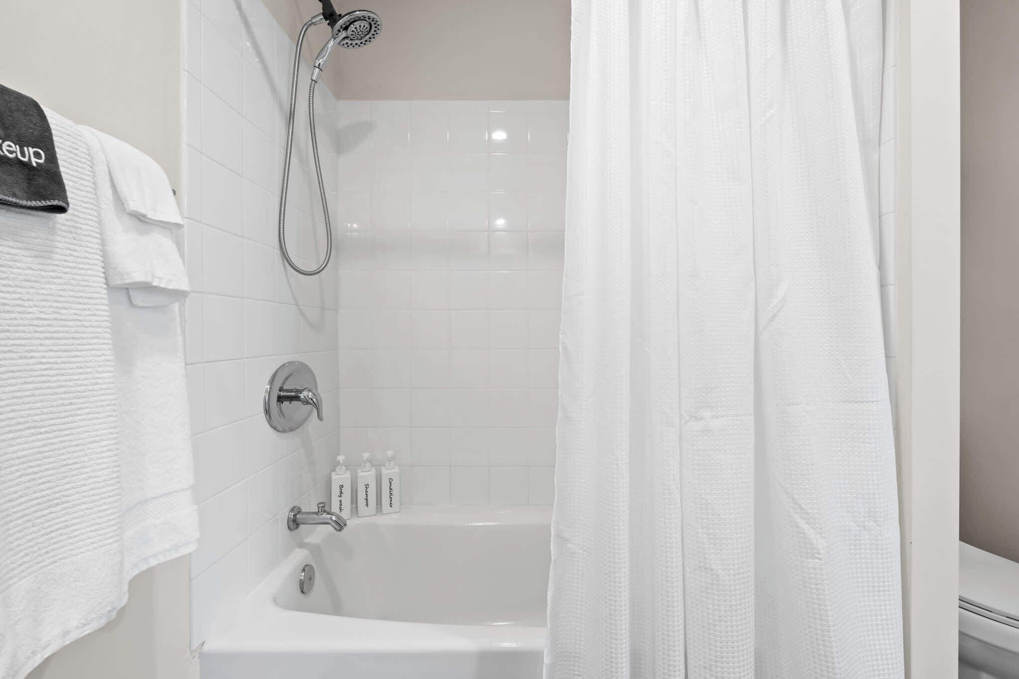 A bathroom with a bathtub, a showerhead, and three bottles of toiletries.