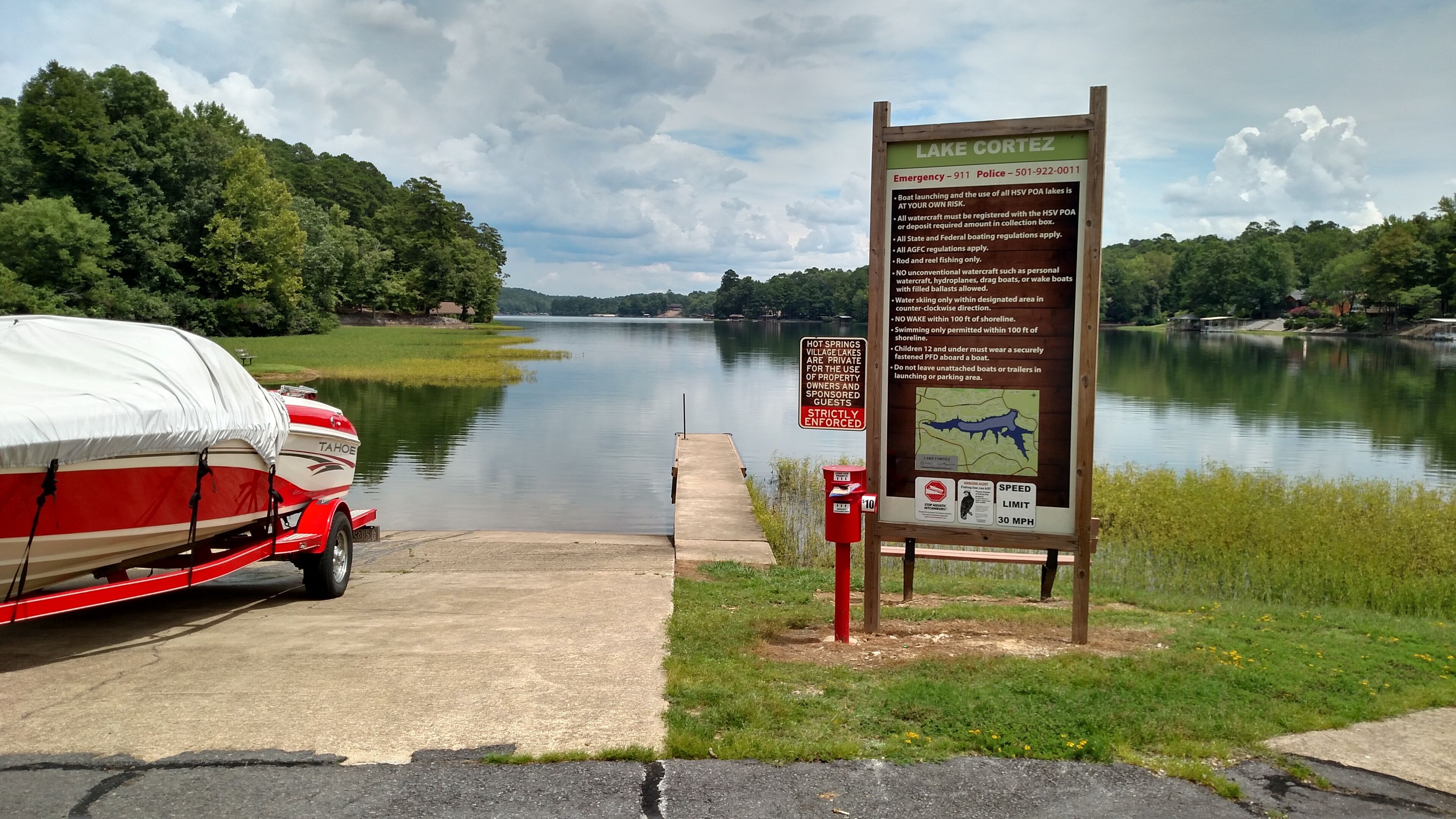 A lake with a covered boat docked at the edge, a signboard with boating regulations, and a speed limit sign.