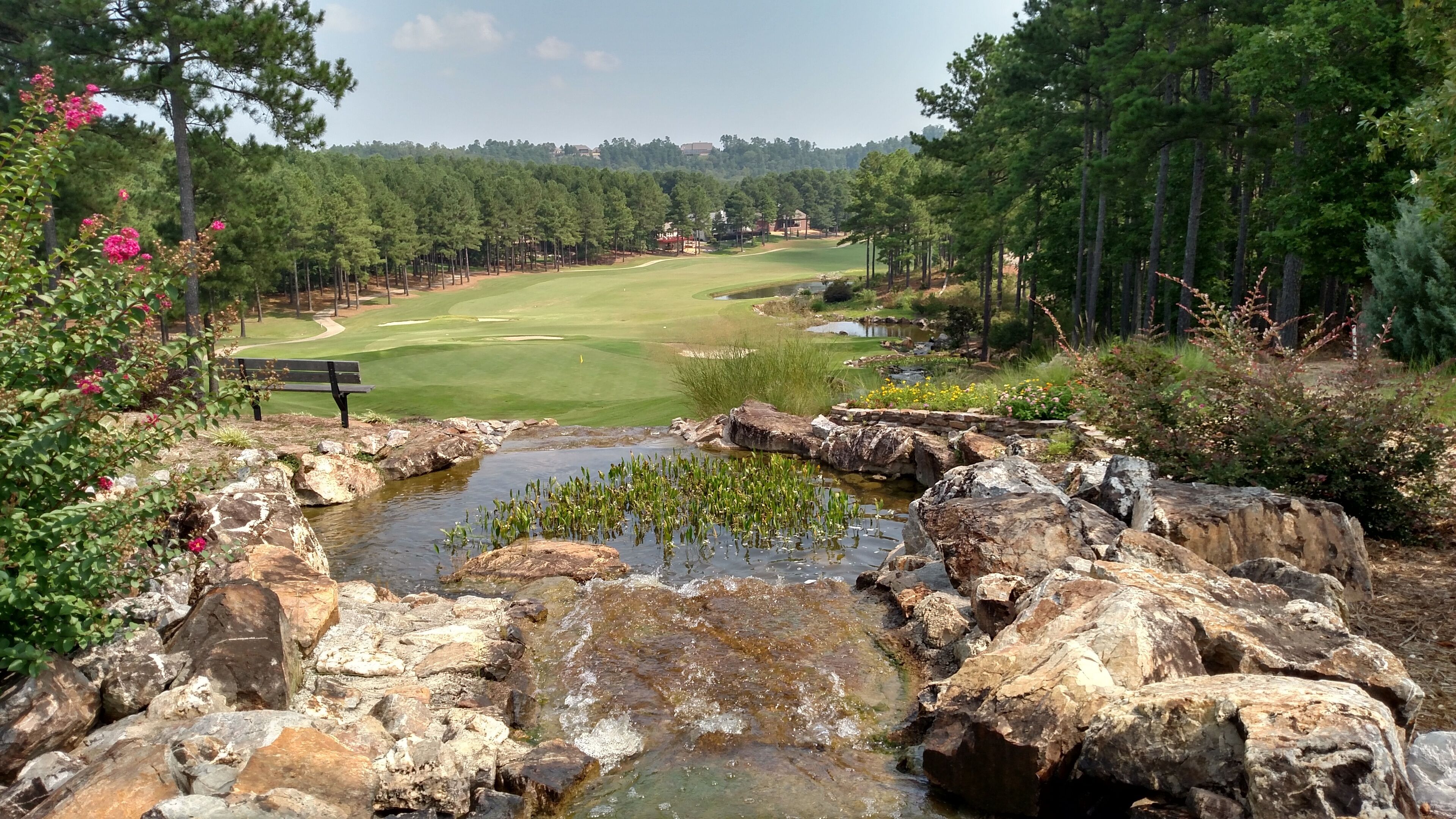 Een golfbaan met een rotsriviertje, bomen en een bankje.