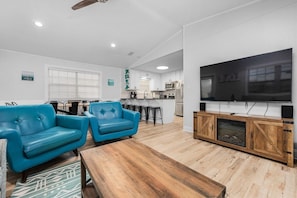 Relax in the spacious living room with a central seating area, flat-screen TV, and kitchen.