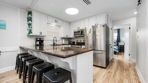 A modern kitchen with white cabinetry, a granite countertop, and stainless steel appliances. There are bar stools and a window with blinds. - 1min Walk To The Beach, Private Heated Pool, Pet Friendly, Zula Dreams Destin (Destin)