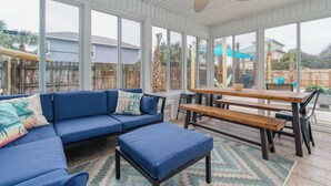 A covered patio with a blue sofa, wooden benches, and large windows offering views of the backyard. - 1min Walk To The Beach, Private Heated Pool, Pet Friendly, Zula Dreams Destin (Destin)