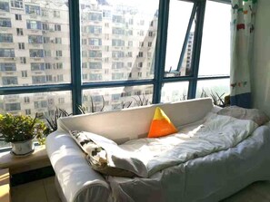 A bedroom with a large window, a sofa bed, a potted plant, and a view of a building. - Golden guesthouse (Beijing)