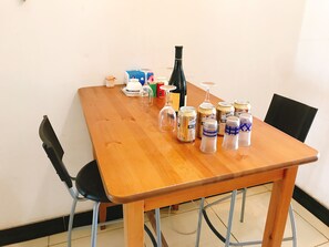 A wooden dining table with various items including a wine bottle, glasses, and cans. - Golden guesthouse (Beijing)