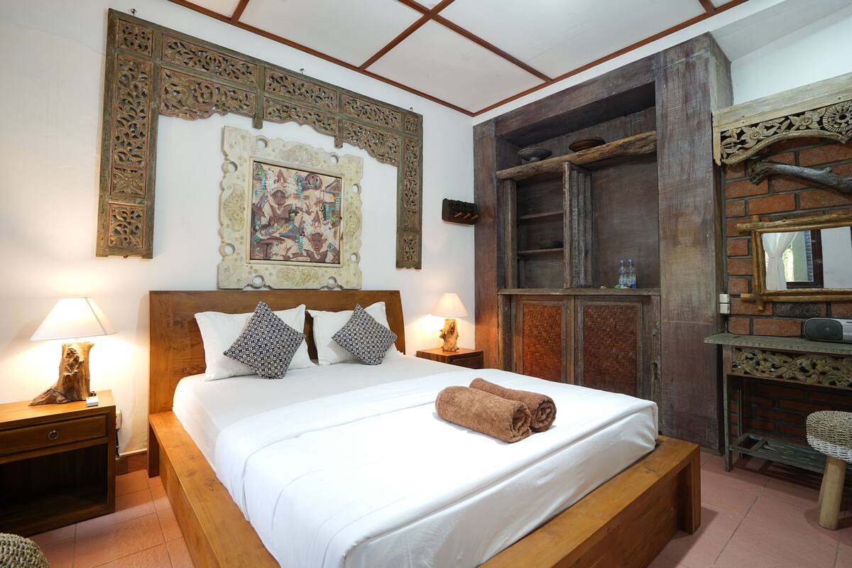 A neatly made bed with a rolled towel, wooden headboard, and decorative wall art.