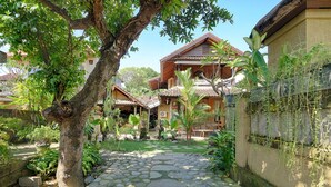 Une cour avec un chemin pavé de pierres, un grand arbre et des bâtiments traditionnels en bois, surmontés de toits en tuiles.