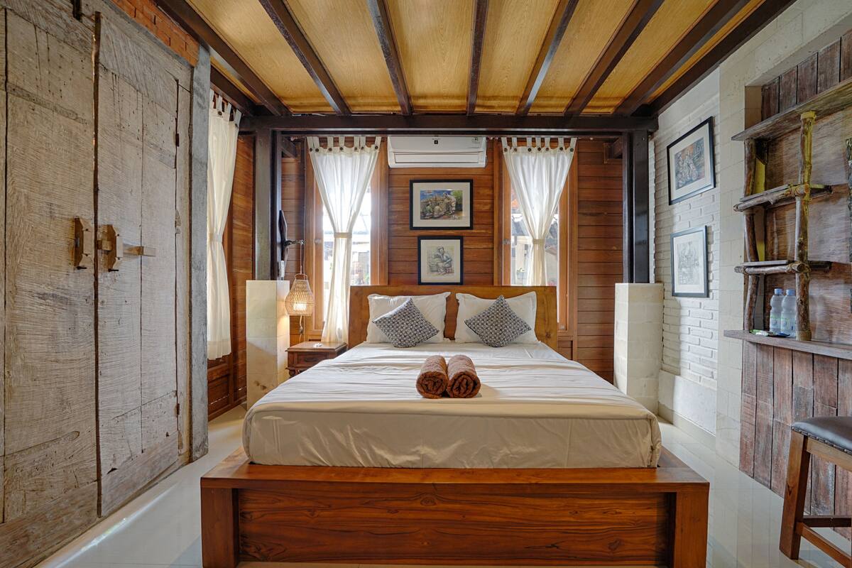 A wooden-framed bedroom with a bed, curtains, and framed pictures on the wall.