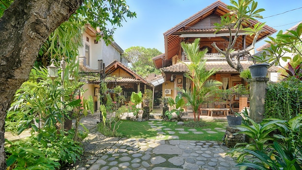 Une maison traditionnelle avec un chemin de pierre menant à l’entrée, entourée d’une végétation luxuriante et d’un jardin bien entretenu.