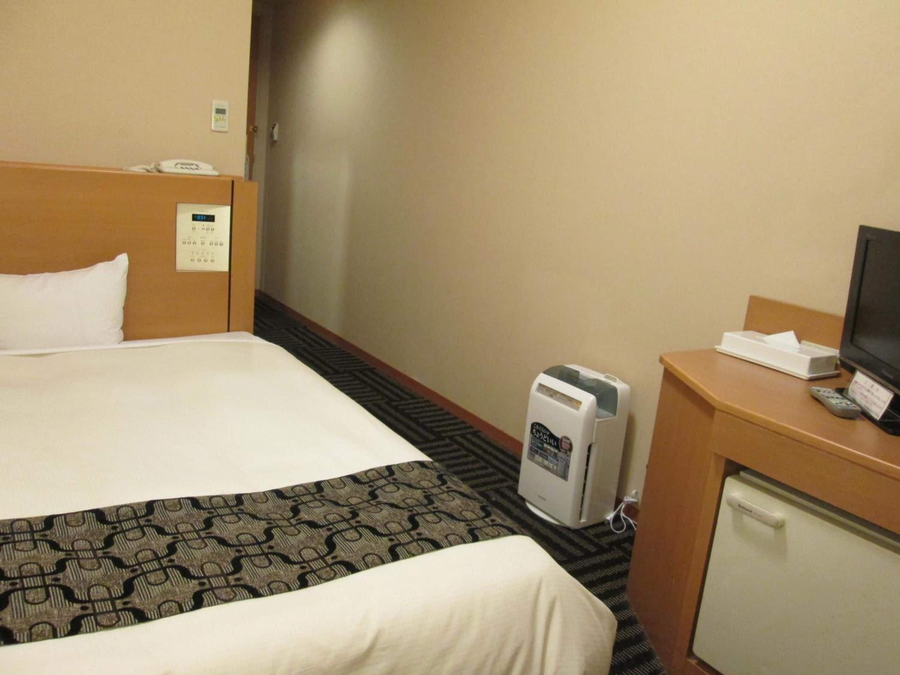 Une chambre d’hôtel équipée d’un lit, d’un bureau avec une télévision, d’un mini-réfrigérateur et d’un téléphone.