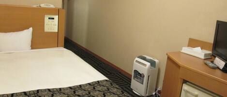 A hotel room with a bed, a desk with a television, a mini-fridge, and a telephone.