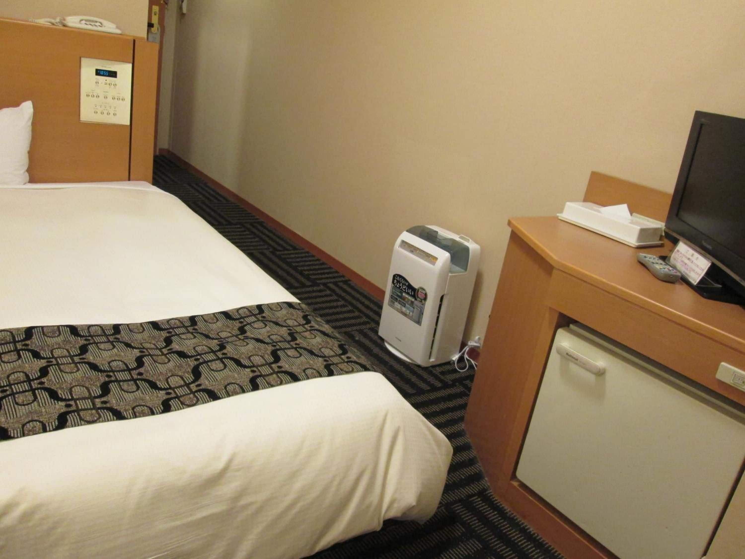 A hotel room with a bed, a desk with a television, a heater, and a telephone.